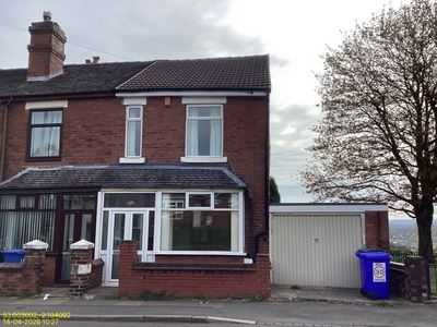 Red-brick end terrace with a side garage and a wheelie bin by the gate